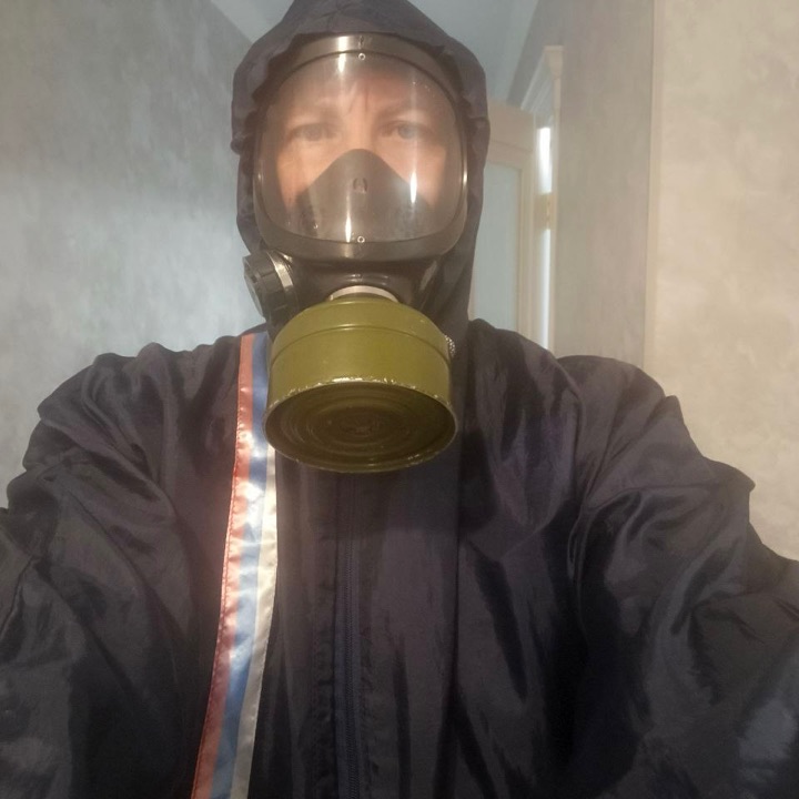 Дезинфектор в противогазе и спецодежде в коридоре квартиры